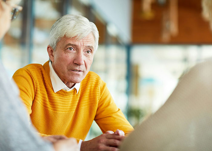 Hombre mayor con suéter amarillo conversando seriamente, ilustrando situaciones difíciles con suegras en reuniones familiares.