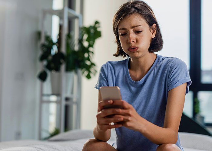 Mujer con expresión preocupada revisando su teléfono, reflejando lo que tiene que soportar con sus suegras.
