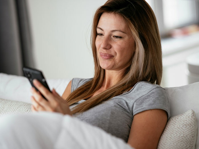 Mujer recostada en sofá mirando su teléfono, ilustrando cómo los teléfonos ayudan a descubrir verdades ocultas. Mujer recostada en sofá mirando su teléfono, ilustrando cómo los teléfonos ayudan a descubrir verdades ocultas.