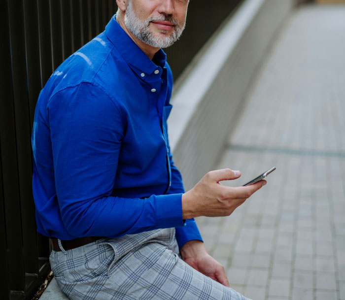 Hombre con camisa azul sentado, usando teléfono móvil para descubrir verdades ocultas en su entorno cotidiano. Hombre con camisa azul sentado, usando teléfono móvil para descubrir verdades ocultas en su entorno cotidiano.