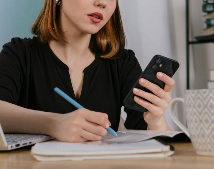 Mujer usando teléfono móvil y tomando notas, ilustrando cómo los teléfonos ayudan a descubrir verdades ocultas. Mujer usando teléfono móvil y tomando notas, ilustrando cómo los teléfonos ayudan a descubrir verdades ocultas.