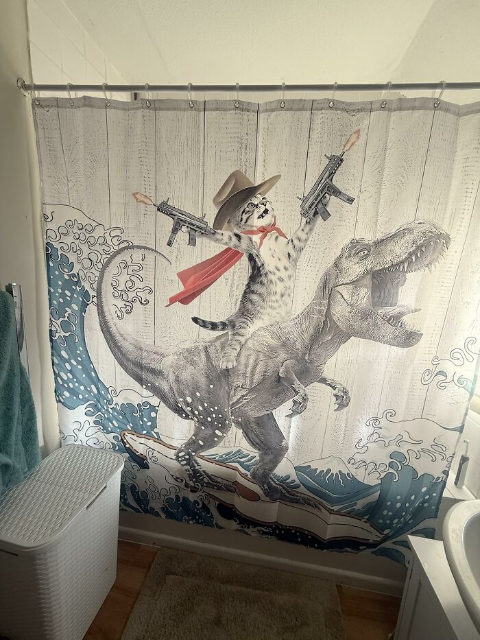 Cortina de baño con diseño ridículo de gato armado montando dinosaurio, inversión extraña y atractiva encontrada online.