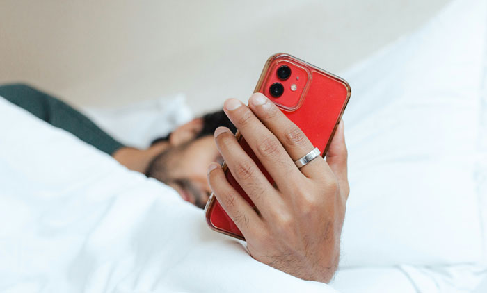 Persona en cama sosteniendo un teléfono rojo, ilustrando cómo los teléfonos ayudaron a descubrir verdades ocultas. Persona en cama sosteniendo un teléfono rojo, ilustrando cómo los teléfonos ayudaron a descubrir verdades ocultas.