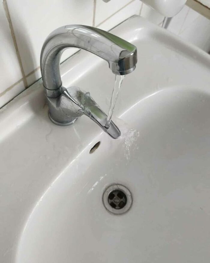 Grifo con doble salida de agua fallido causando desperdicio, ejemplo divertido de fallos de construcción en lavabo blanco.