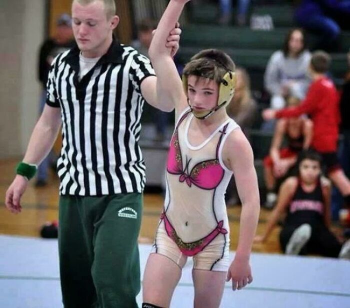Joven luchador con uniforme hilarante que imita bikini, levantando el brazo en señal de victoria en lucha libre.