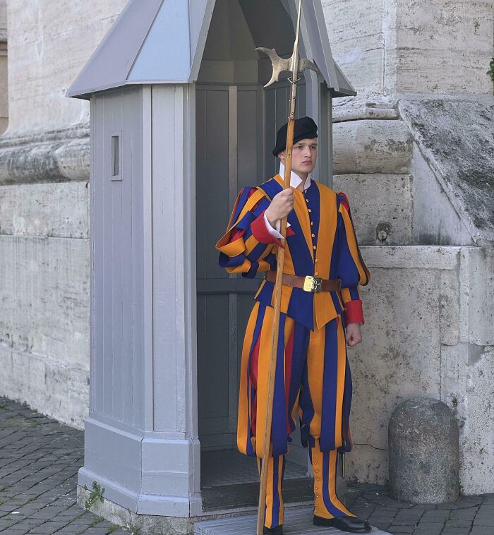 Guardia suizo vestido con uniforme colorido y llamativo, parado en un puesto de vigilancia, diseño de uniformes curioso.