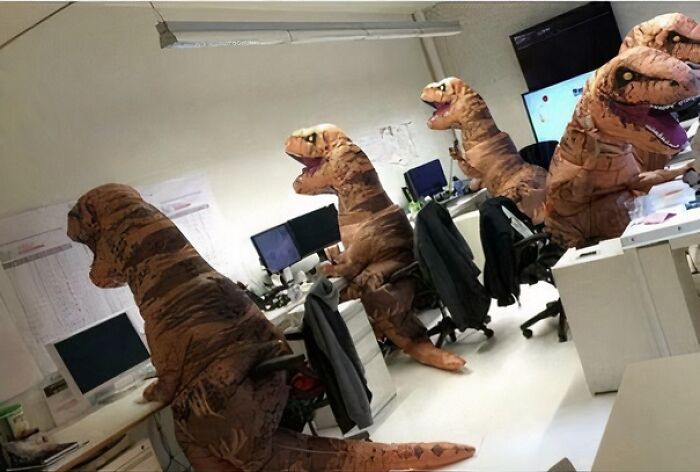 Varias personas en oficinas con uniformes graciosos de dinosaurios que provocan dudas sobre su diseño.