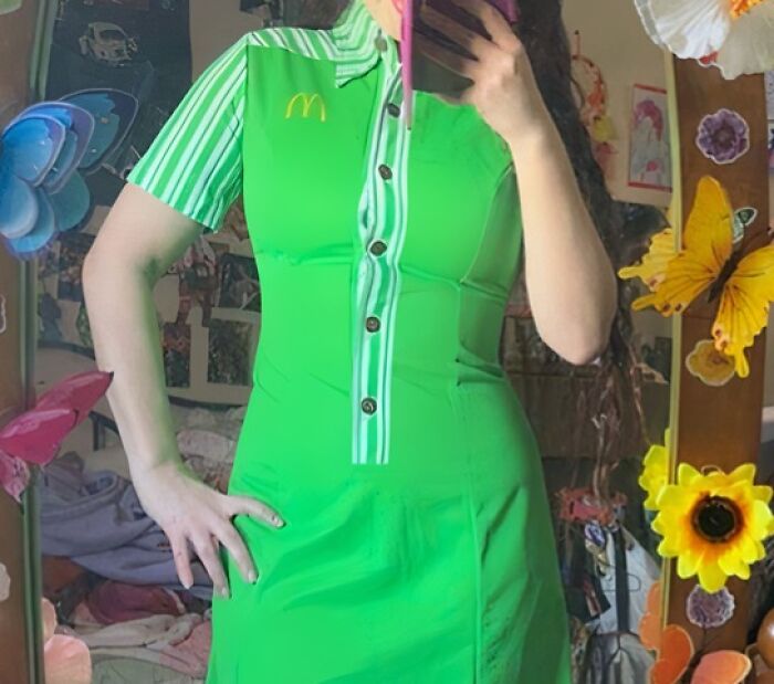 Mujer con uniforme verde brillante de McDonald's frente a un espejo, mostrando un diseño de uniforme hilarante y cuestionable.