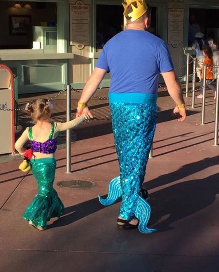 Hombre y niña con disfraces de sirenas en parque de atracciones mostrando gran sentido del humor y diversión familiar.