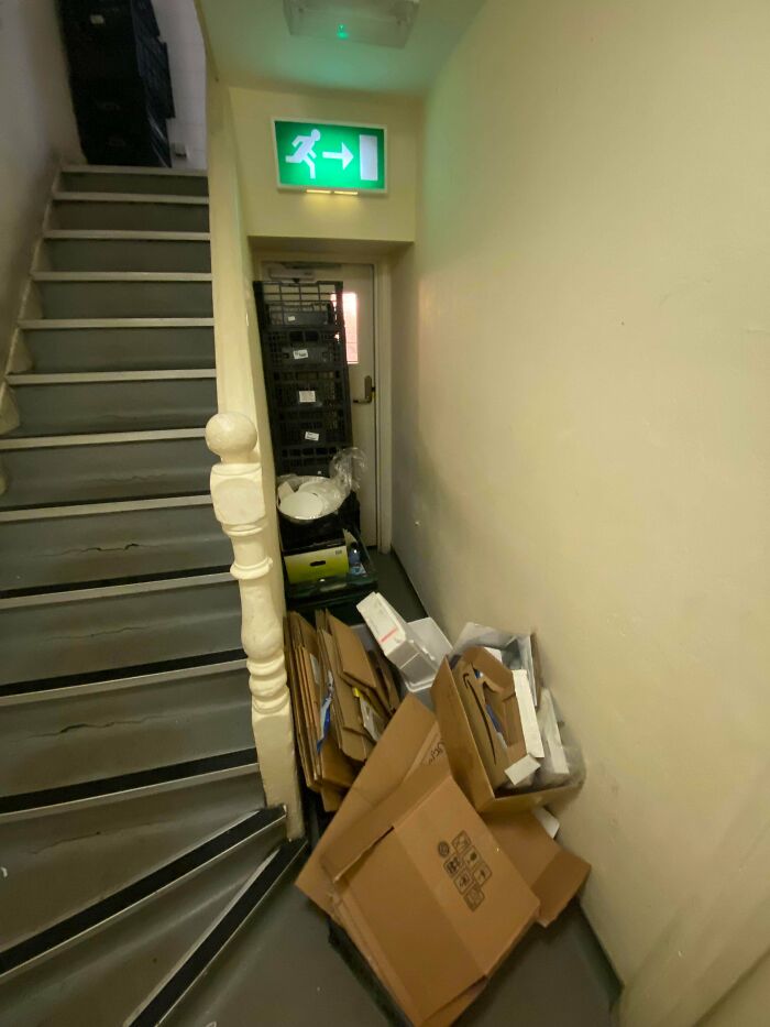 Escalera bloqueada con cajas y basura obstaculizando salida de emergencia en lugar de trabajo con jefes pésimos.