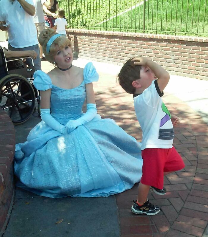 Niño con gesto divertido junto a mujer disfrazada de princesa en parque de diversiones, capturando momentos con humor.
