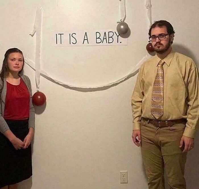 Pareja posando frente a un cartel minimalista que dice "It is a baby" en una foto extraña y curiosa.