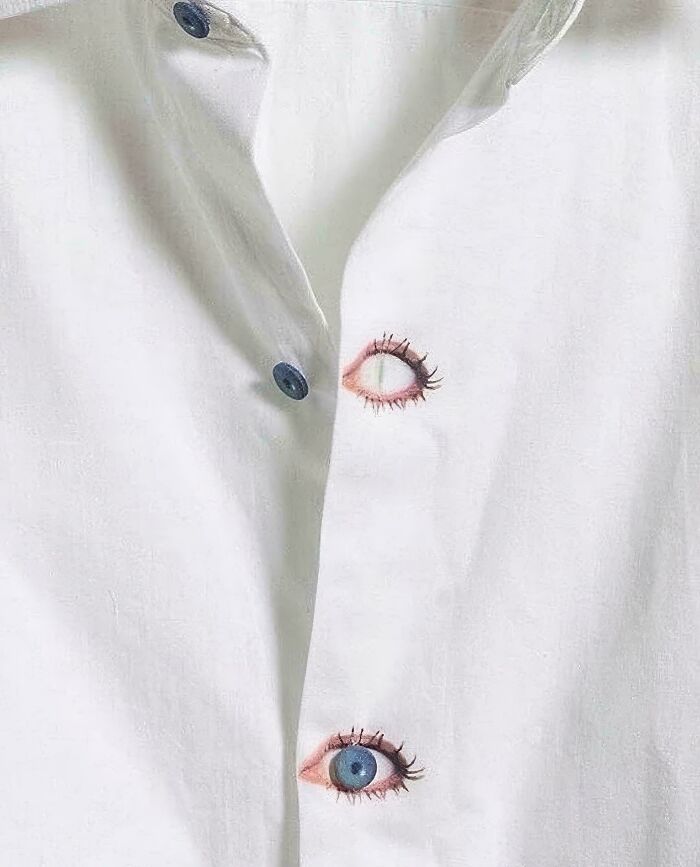 Camisa blanca con botones que parecen ojos pintados, imagen rara y extraña que llama la atención.