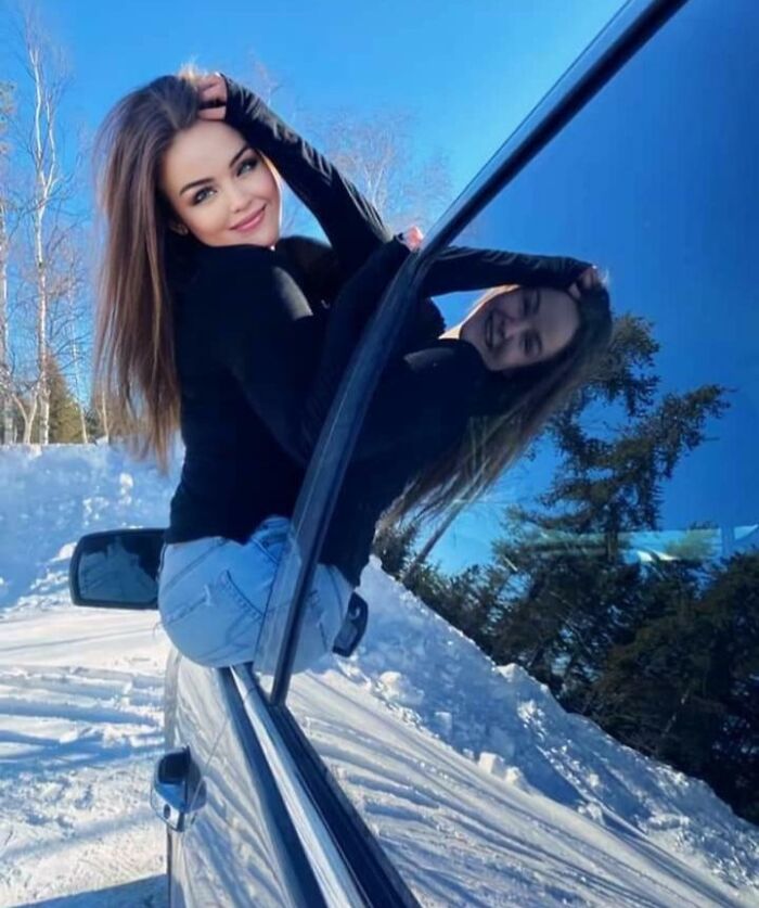 Mujer posa creativamente afuera del auto con reflejo, una de las fotos falsas que confunden la realidad.