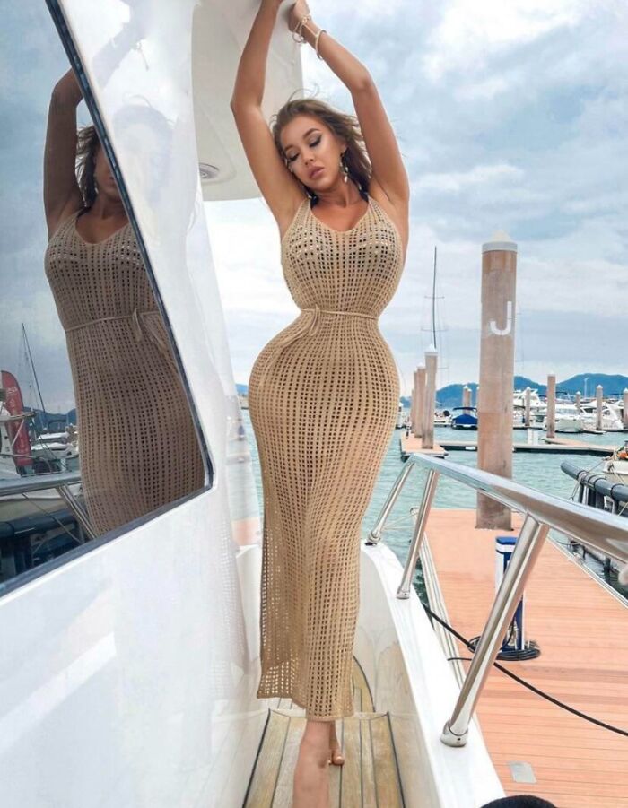 Mujer con vestido ajustado y figura distorsionada posando en un yate, ejemplo de fotos falsas y fuera de la realidad.