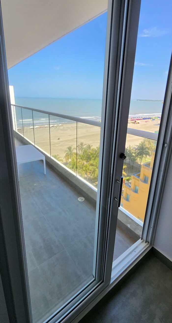Vista de balcón con puerta de vidrio hacia playa y palmeras en fotos de vacaciones que no salieron como se esperaba