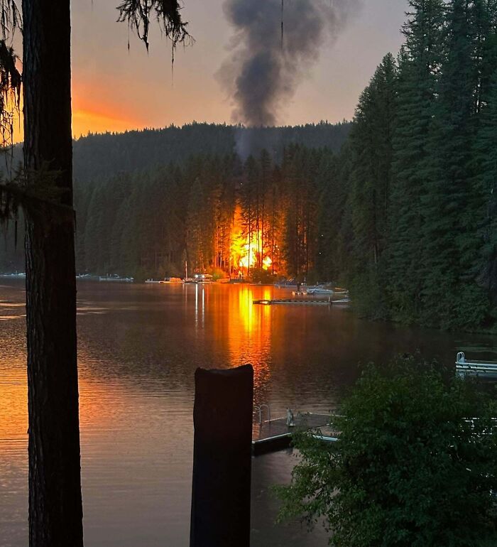 Incendio inesperado en bosque junto a lago, reflejando fuego en el agua en unas fotos de vacaciones sorprendentes.