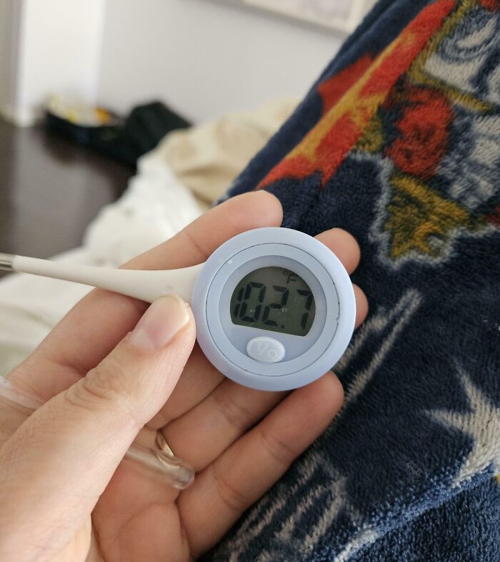 Termómetro digital en mano mostrando temperatura 102.7°F durante vacaciones que no salieron como se esperaba.