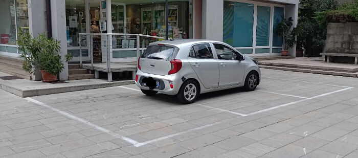 Coche plateado mal estacionado en una plaza vacía, ejemplo de personas actuando mal y siendo expuestas.
