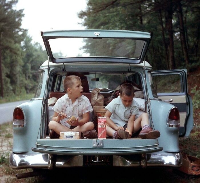 Dos niños sentados en el maletero abierto de un coche antiguo, disfrutando un picnic en un entorno natural, zapatos visibles. Dos niños sentados en el maletero abierto de un coche antiguo, disfrutando un picnic en un entorno natural, zapatos visibles.