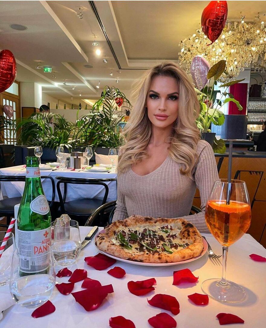 Mujer en restaurante con pizza y bebida, mostrando belleza real y natural más allá de Instagram.