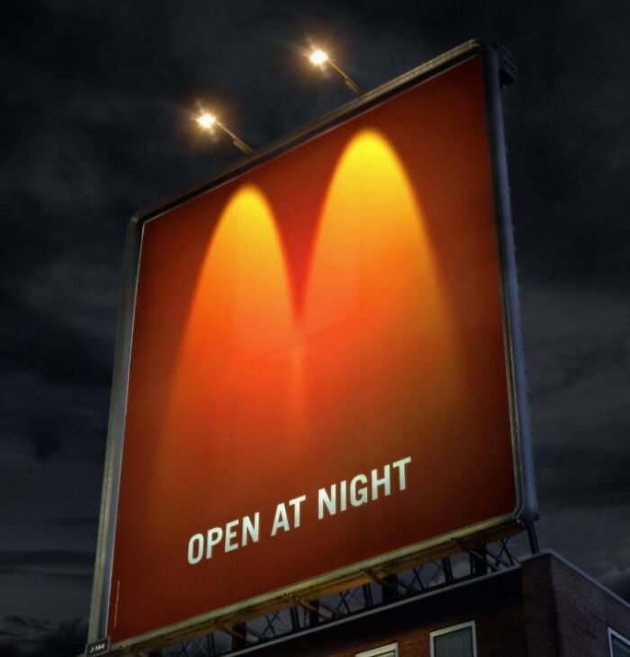 Cartel publicitario divertido y brillante iluminado de noche con texto en inglés "Open at night" destacado en fondo naranja.