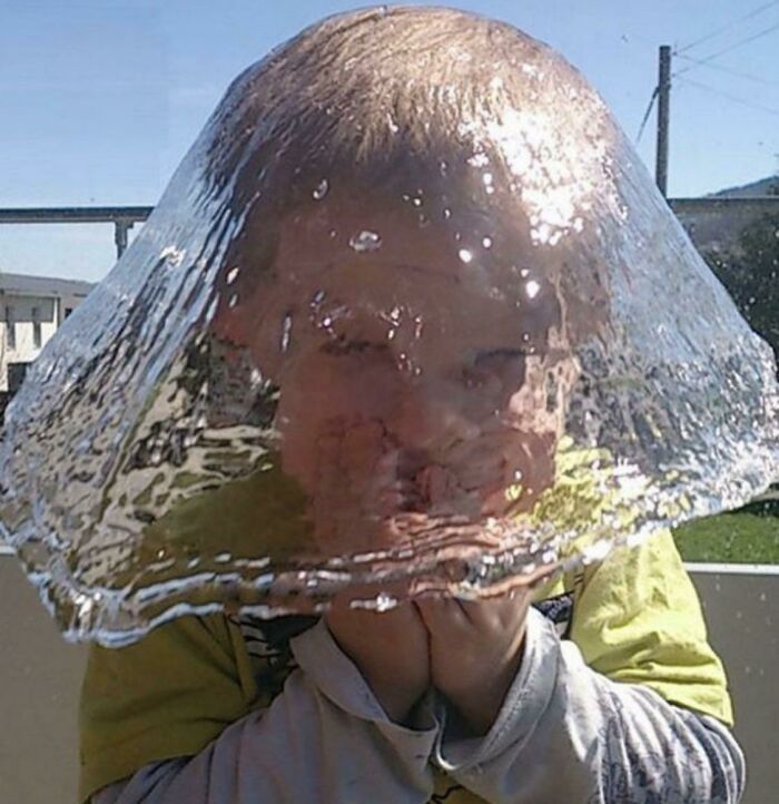 Niño capturado en el momento antes del desastre con una burbuja de agua cubriendo su cabeza de forma divertida y sorprendente.