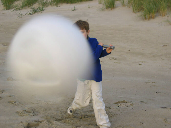 Niño en la playa bateando una pelota gigante captura el momento justo antes del desastre divertido.
