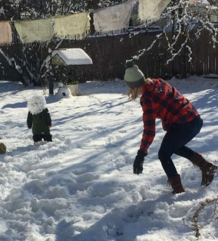 Niña lanzando bola de nieve a un niño, capturando el momento justo antes del desastre en un jardín nevado y soleado.