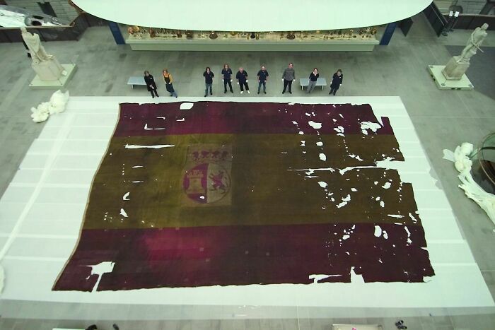 Personas junto a una bandera antigua mostrando el tamaño real del cuerpo humano comparado con objetos grandes, cuerpo humano.