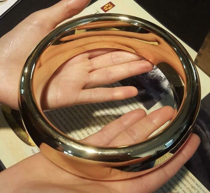 Manos sosteniendo un espejo reflectante circular que muestra la explicación del tamaño humano real.