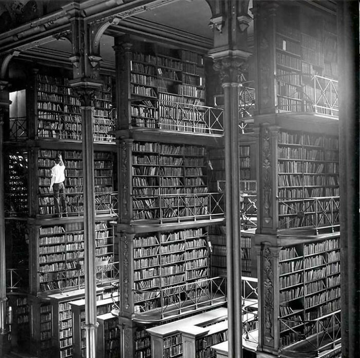 Persona en biblioteca antigua mostrando el tamaño real de los estantes en comparación con el cuerpo humano.