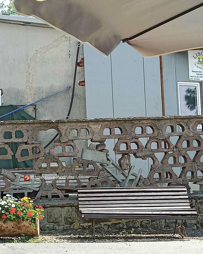 Muro de construcción defectuoso con bloques mal colocados y banco frente a flores en un espacio exterior.