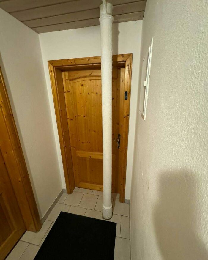 Columna obstructiva frente a una puerta de madera en un pasillo, ejemplo de fallos de construcción divertidos.