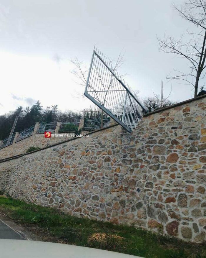 Reja suspendida sin soporte adecuado en muro de piedra, mostrando un divertido fallo de construcción llamativo y absurdo.