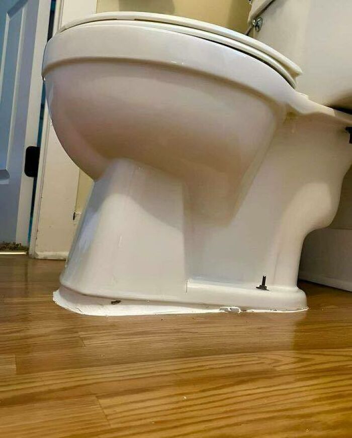 Inodoro instalado sobre suelo de madera con acabado irregular y evidencia de fallos de construcción visibles en el borde.