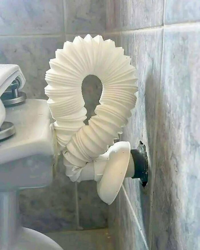Tubería flexible instalada incorrectamente en baño, un fallo de construcción divertido y poco funcional junto a un inodoro.