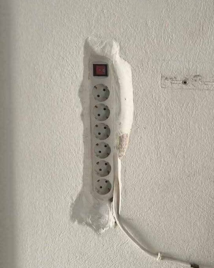 Enchufe múltiple mal instalado en pared, mostrando un claro error de construcción divertido y problemático.