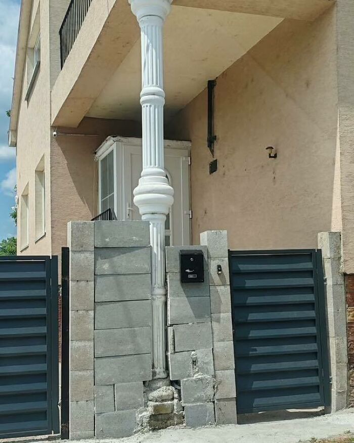 Columna decorativa sosteniendo un muro mal construido con bloques de cemento y puerta metálica en construcción fallida.