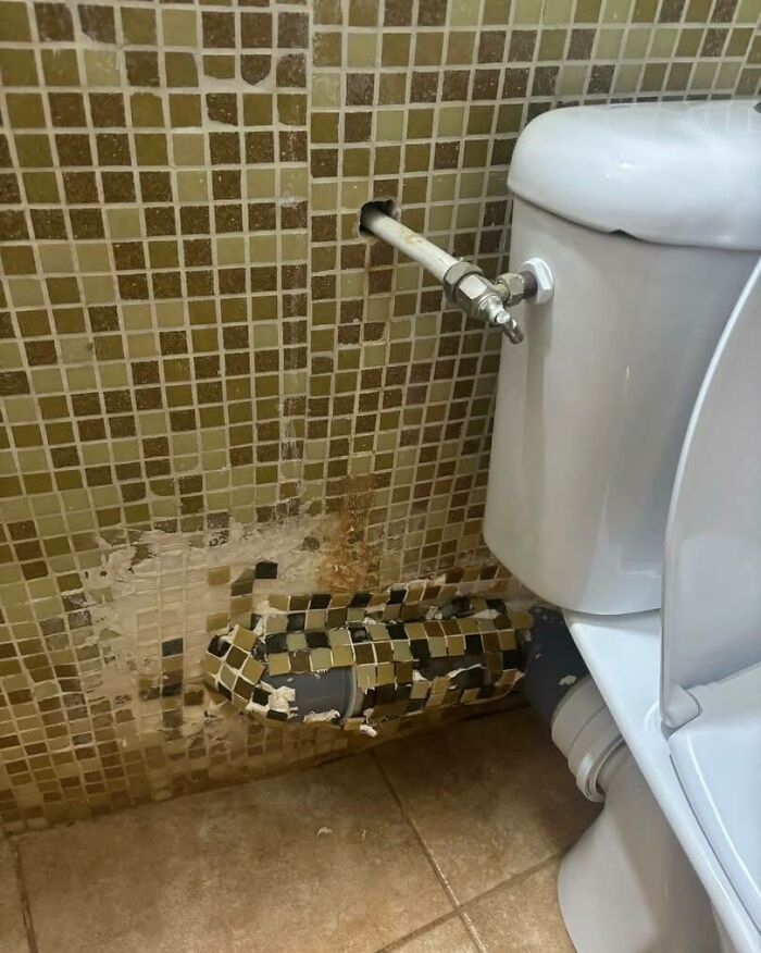 Tubería mal instalada con azulejos mal colocados y daños visibles en pared junto a inodoro, ejemplos de fallos de construcción.