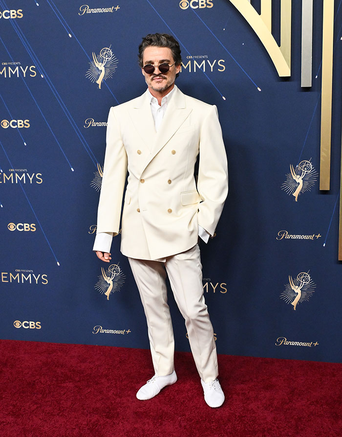 Hombre con traje blanco y gafas de sol en la alfombra roja, destacando en moda en los Emmys 2025.
