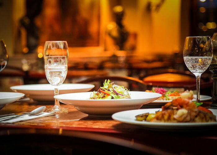 Mesa elegante con platos de comida y copas de agua, mostrando a personas que parecen poco inteligentes en un restaurante.
