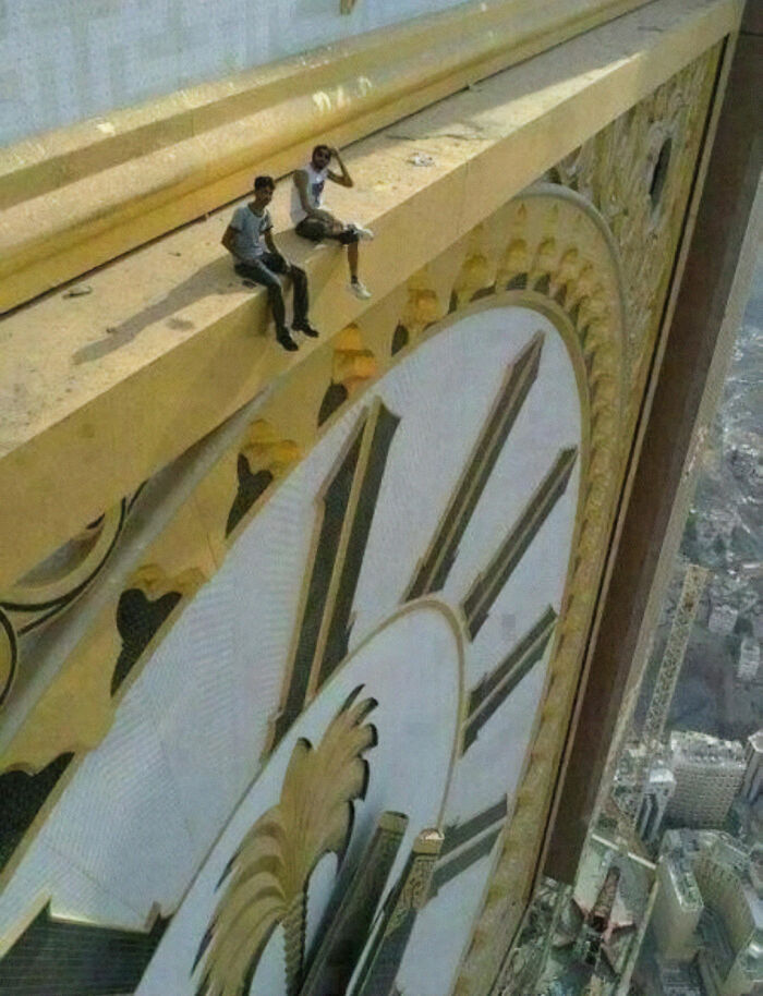 Dos personas sentadas en la parte superior de un reloj gigante mostrando el tamaño verdadero con el cuerpo humano.