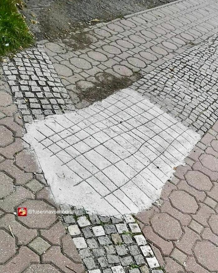 Parche de cemento mal hecho sobre acera de adoquines mostrando divertidos fallos de construcción y errores evidentes.