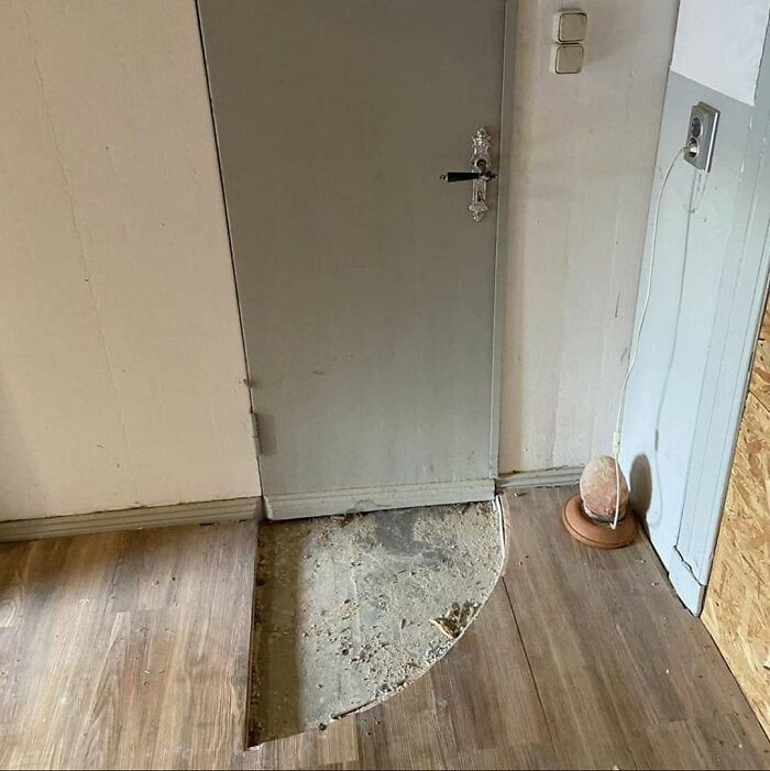 Fallo de construcción con suelo mal instalado frente a puerta gris, ejemplo divertido de fallos de construcción para reír y llorar.