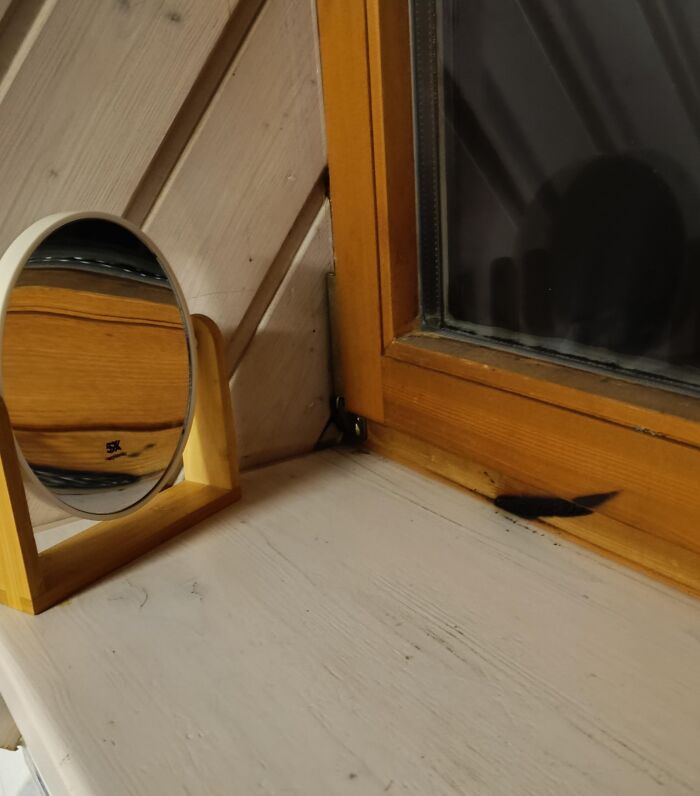 Espejo de mesa frente a ventana de madera mostrando sombra confusa que parece figura peligrosa sin intención.