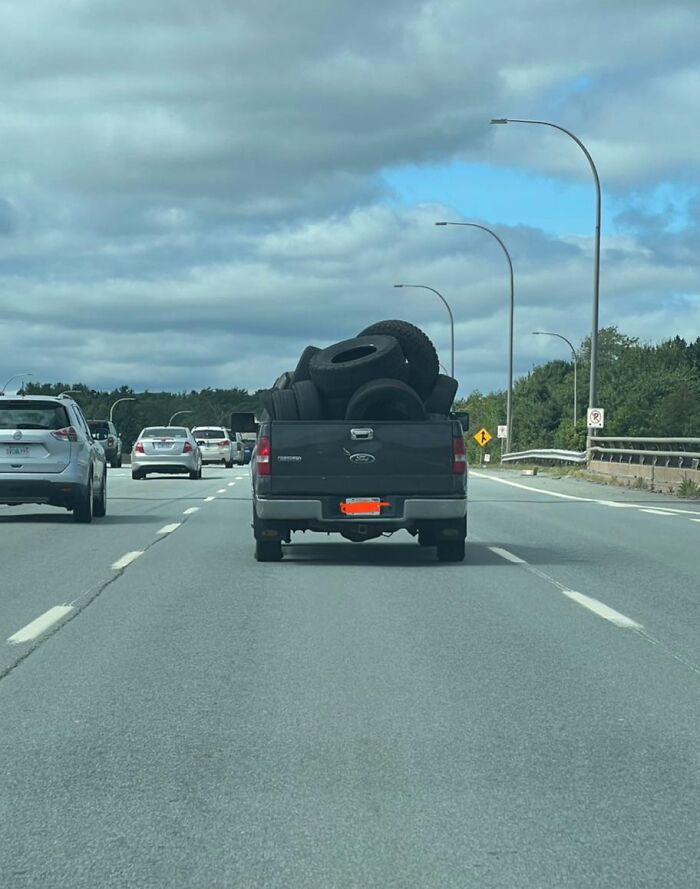 Camioneta cargando neumáticos sin seguridad en carretera transitada, ejemplo de personas haciendo algo peligroso sin saberlo.