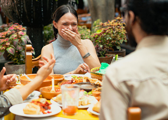 Mujer riendo en comida con amigos, mostrando expresiones que reflejan lo difícil de creer lo tonto que pueden ser algunas personas.