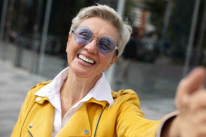 Mujer sonriente con gafas redondas y chaqueta amarilla ilustrando historias de horror de médicos y enfermeras memorables.