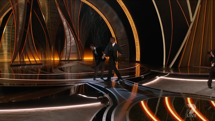 Dos hombres vestidos de traje en un escenario moderno con luces doradas, representando decisiones que arruinaron vidas.
